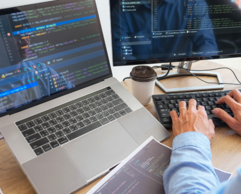 Side View Of Programmer Typing On Keyboard Looking At Many Monitors