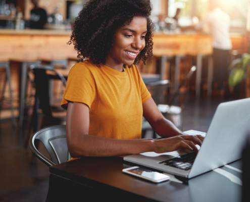 Young Woman In Café Typing On Laptop