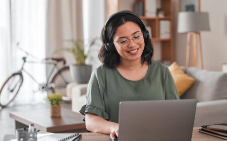 Side view of a smiling woman wearing a headset while staring at a laptop screen