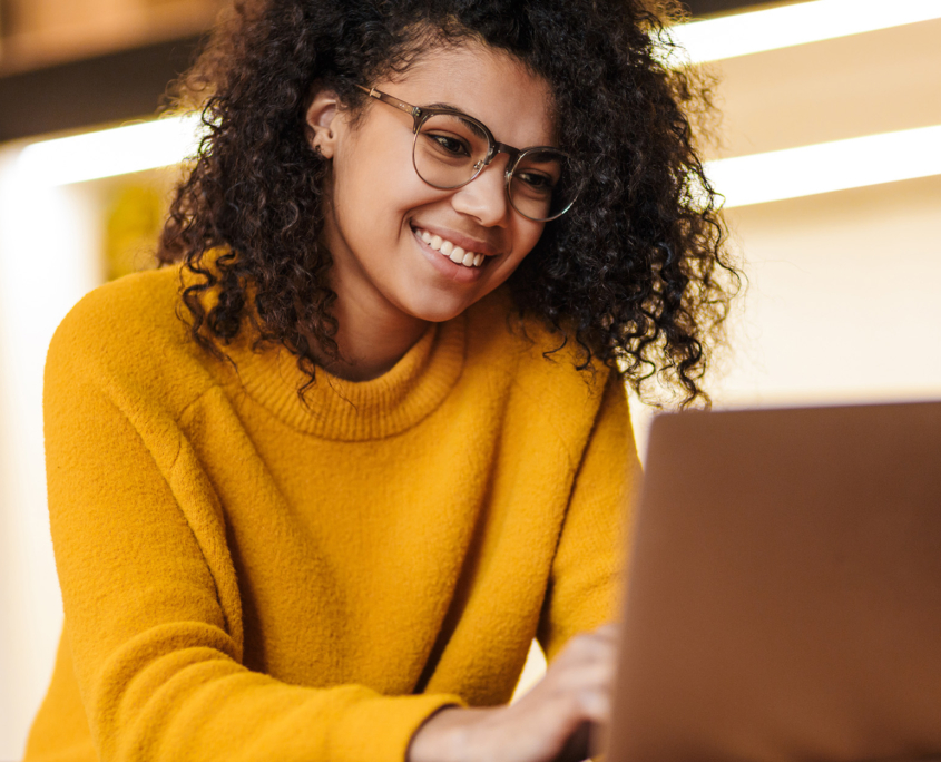 Side View Of Woman With Glasses And Yellow Sweater On Laptop