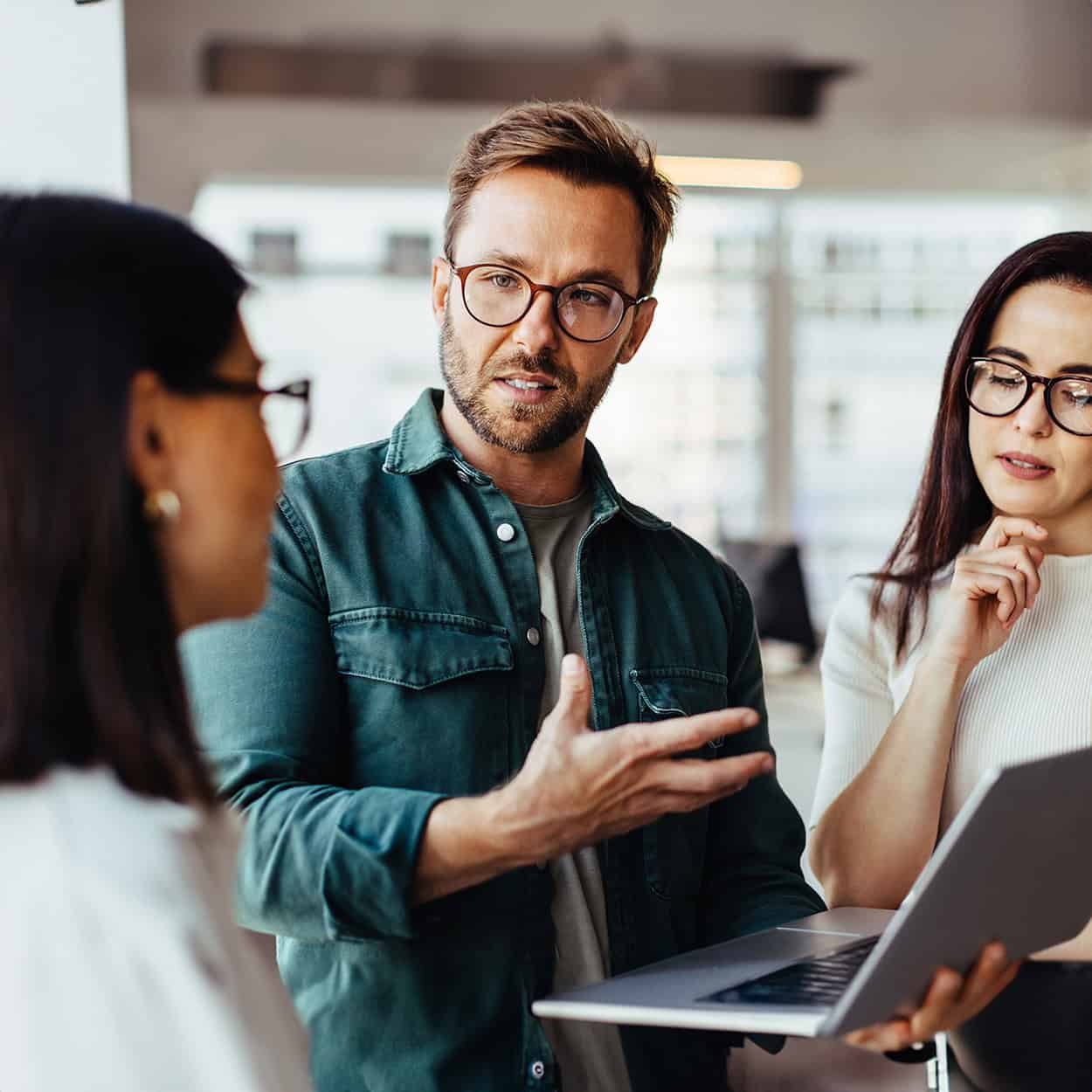 Header Front View Of Man Explaining Something To His Coworkers While Holding Laptop