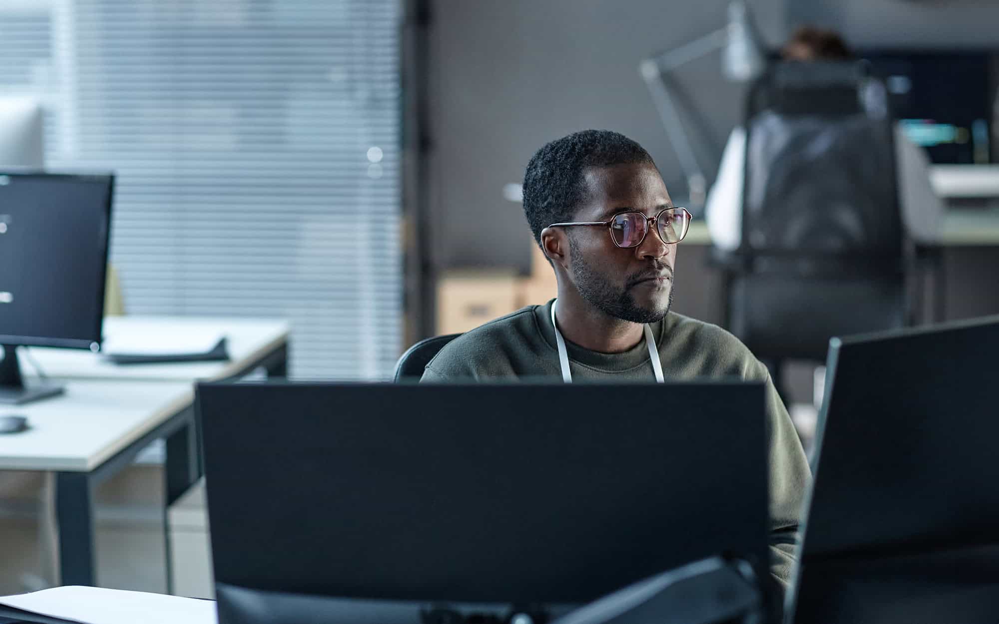 Side View Of Man In Glasses Looking At Computer Screens