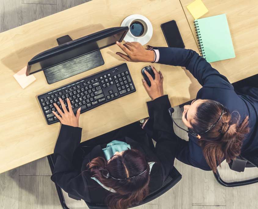 Top Down View Of Two Women In Business Attire Working On Computer At Long Desk