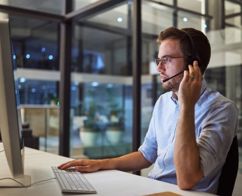 Side view of a man holding a headset while on a call looking at computer screen