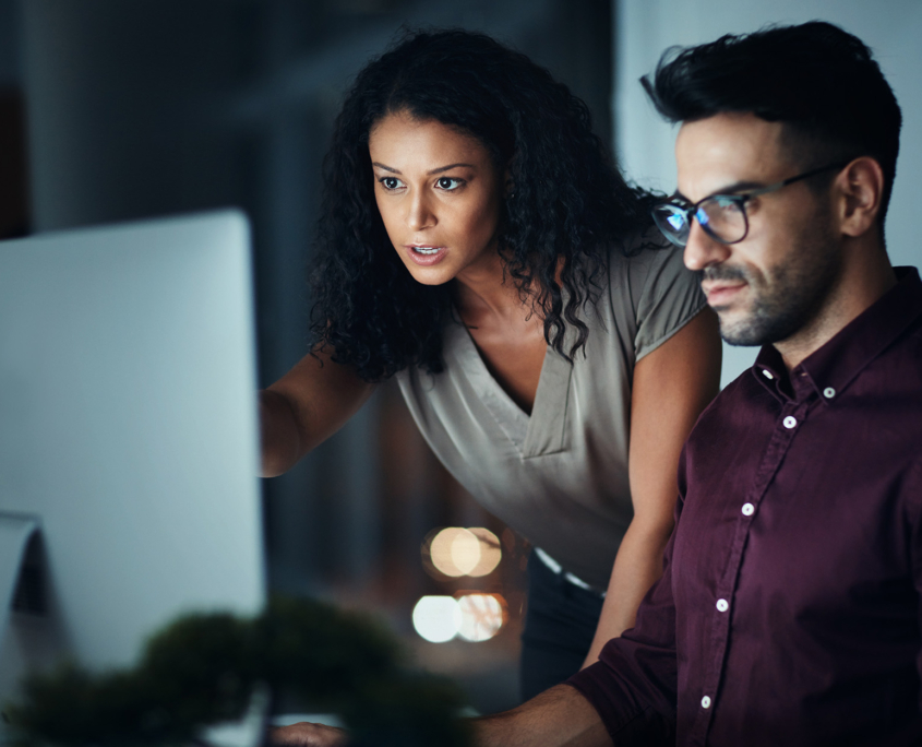 Side View Of Two Coworkers Working On Computer Monitor In Dark Room